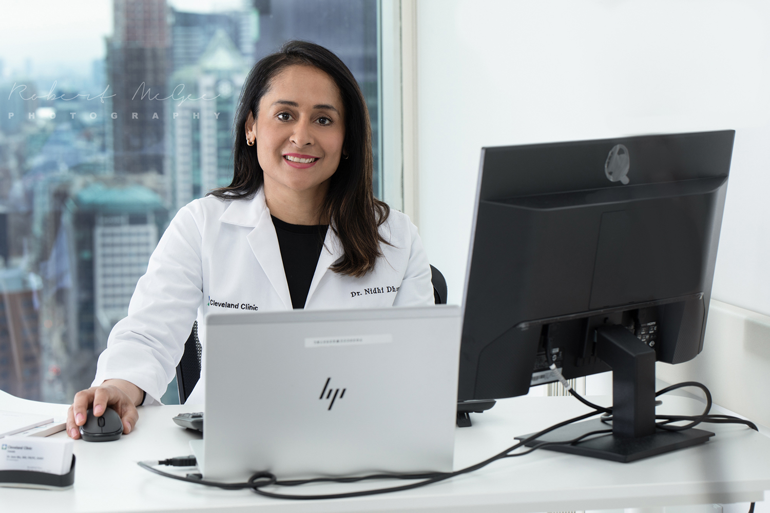 Cleveland clinic doctor sits at desk behind computer with window behind