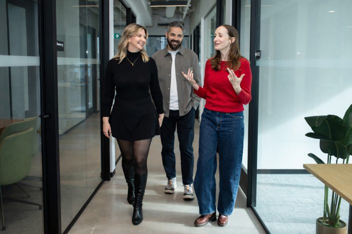 candd photo of three professionals walking together through a modern office hallway.