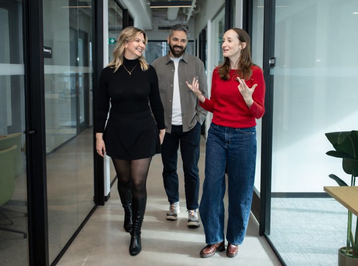 candd photo of three professionals walking together through a modern office hallway.