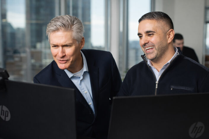 Corporate office photography of two men in business wear working at computer screens, one dressed more casually, modern professional business environment